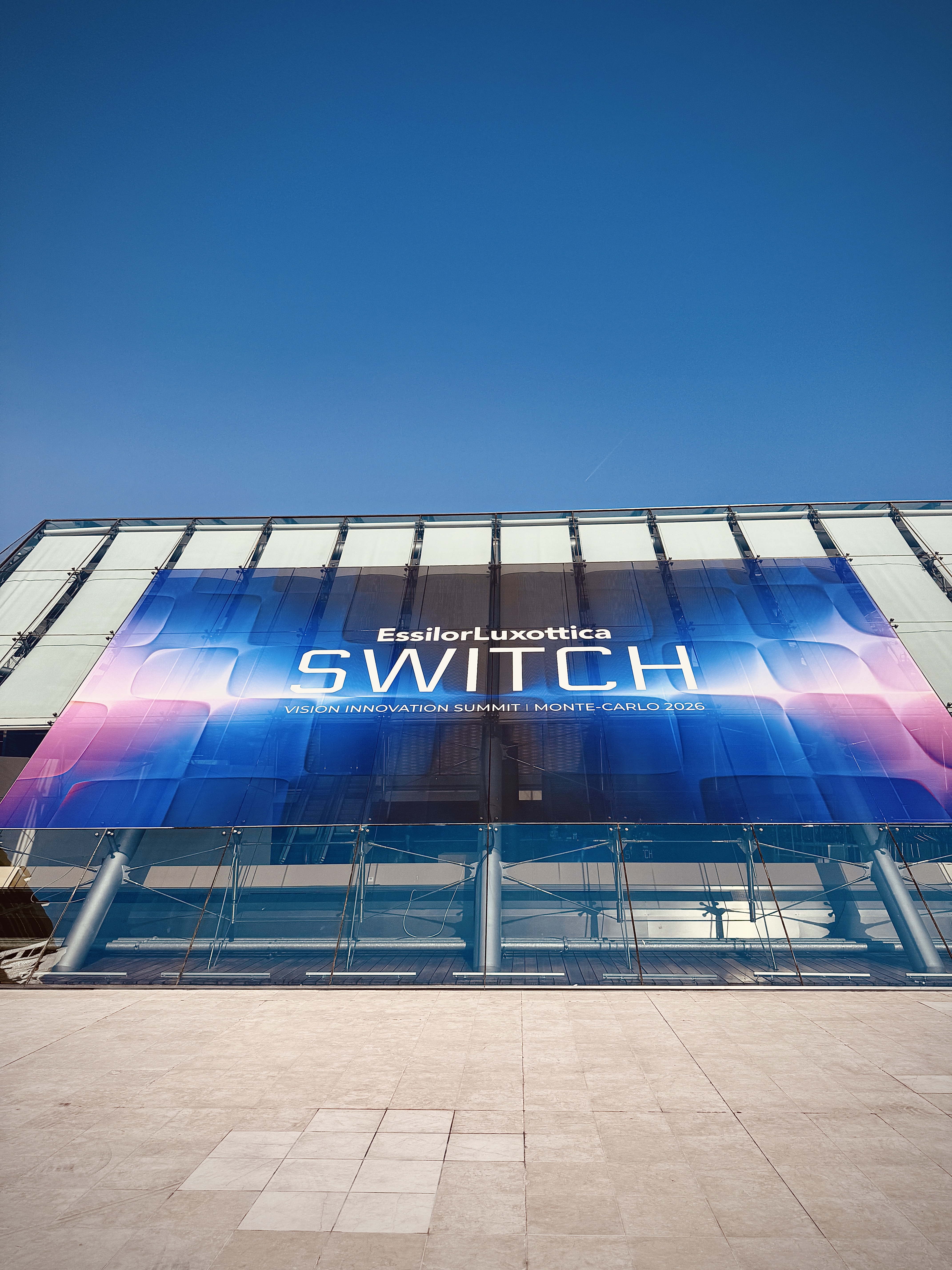 A large banner reading EssilorLuxottica Switch, Vision Innovation Summit, Monte-Carlo 2026 on a glass facade