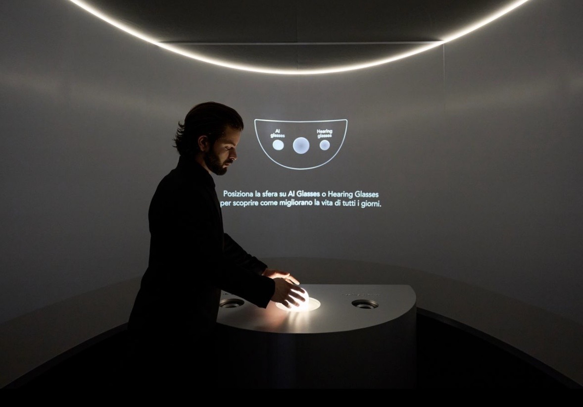 A visitor moving a glowing sphere across a curved console while instructions are projected on the wall behind